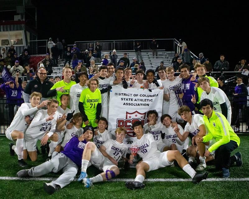 The 2019-20 varsity soccer team posing with their DC state championship banner after defeating Sidwelll Friends 3-0. (Photo by Susan Cowley)