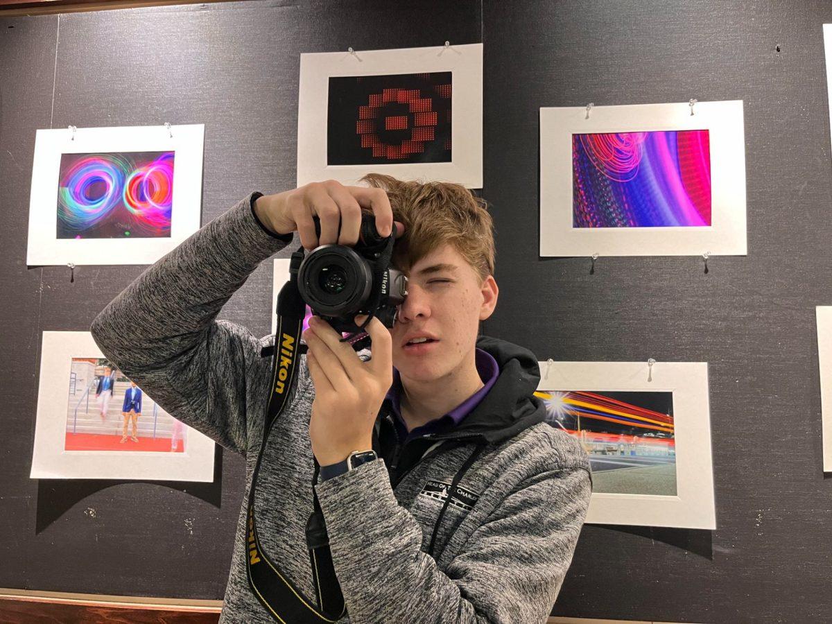 Photography student, Kyle McHugh '24 takes pictures; other art students works are plastered in the background. Photo: Preston Thomas '24